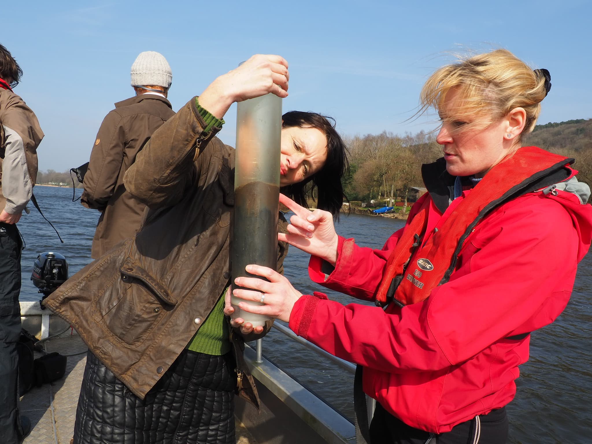 Two female academics looking into a tube with sediment sample inside whilst on a boat